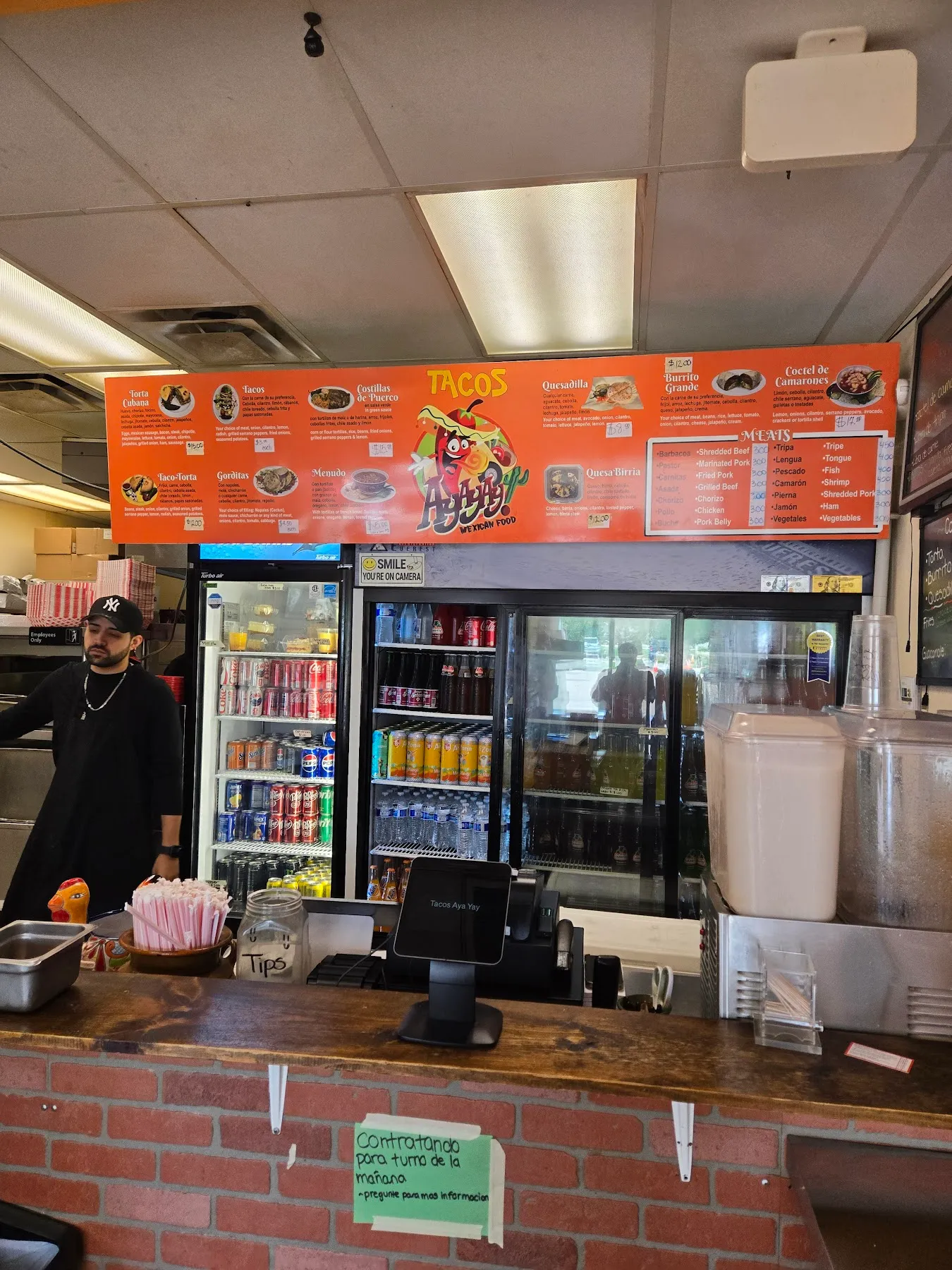 The Tacos Ay Ay Ay counter with the orange menu board listing tacos, tortas, quesadillas, menudo, and the list of meats