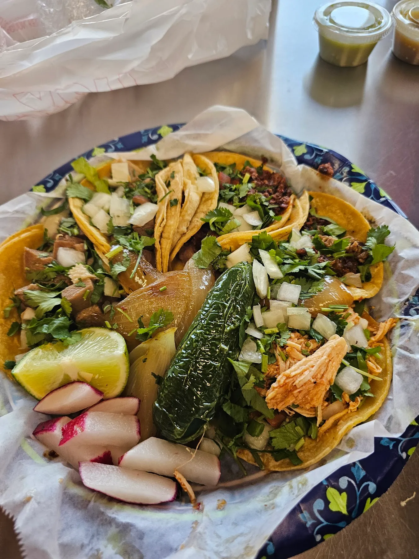 A plate of assorted street tacos topped with cilantro and onion, with a grilled jalapeno, lime, and radish