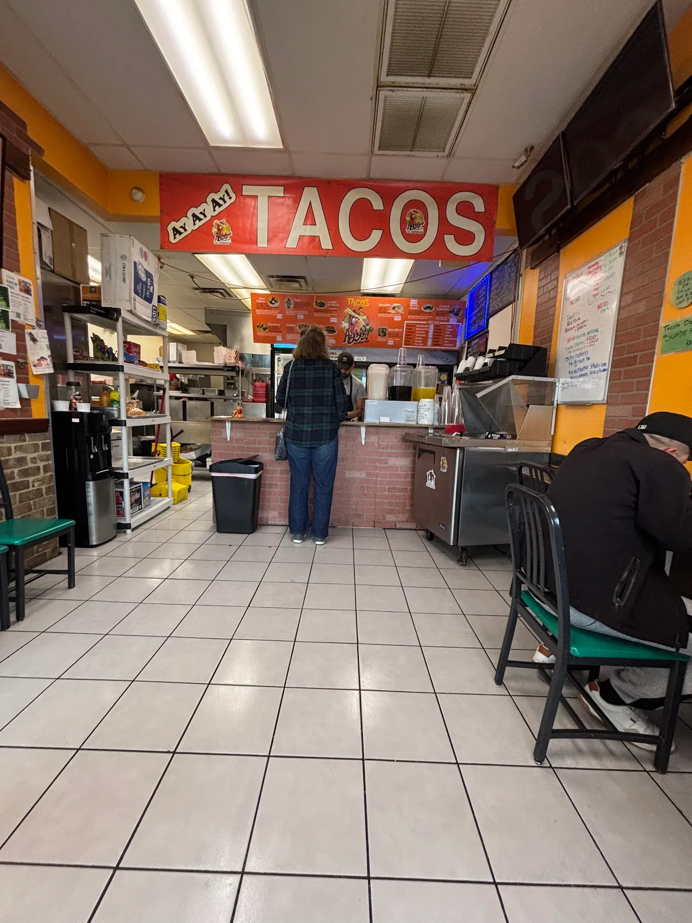 Inside the taqueria with the red Ay Ay Ay! Tacos banner, tile floor, and a customer ordering at the counter